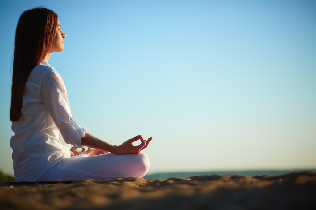 Side view of meditating woman sitting in pose of lotus against blue sky outdoors