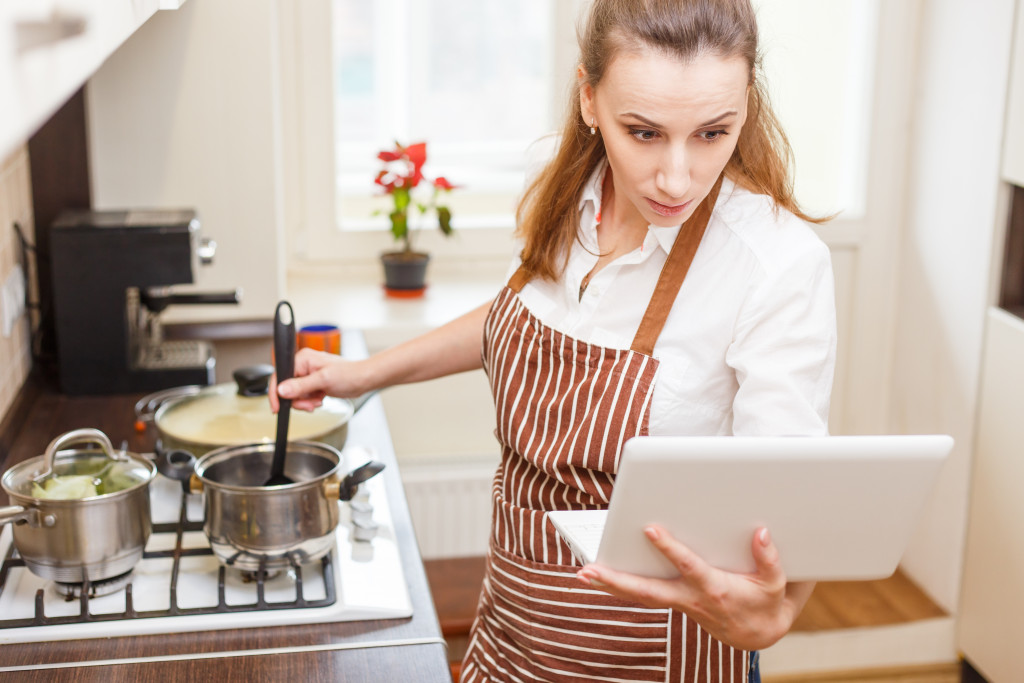 a woman wearing apron in the kitchen looking recipe at a tablet