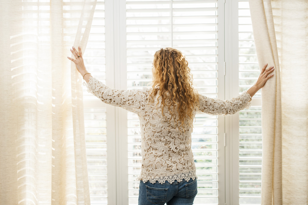 A woman parting the curtains to let in natural light through the windows