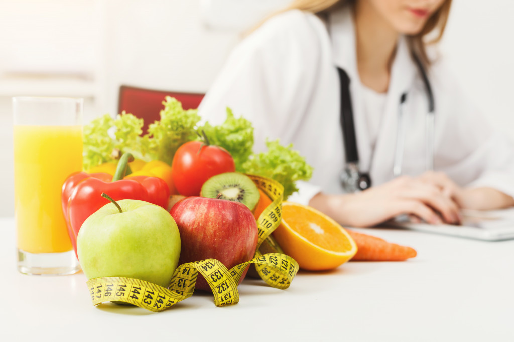 Fruits and vegetables on a table with a female doctor in the background.
