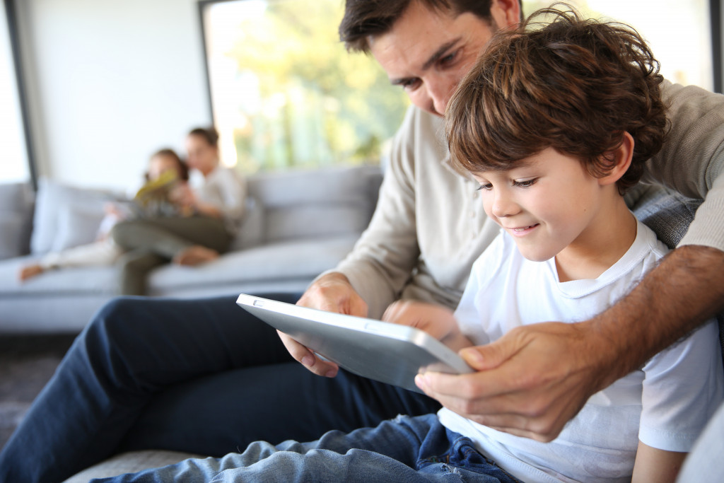 dad playing with son on tablet while relaxing at home