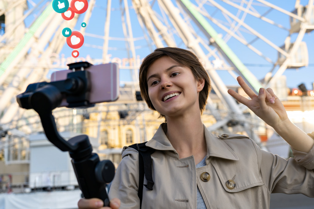 a young woman taking a selfie video in front of a ferris wheel