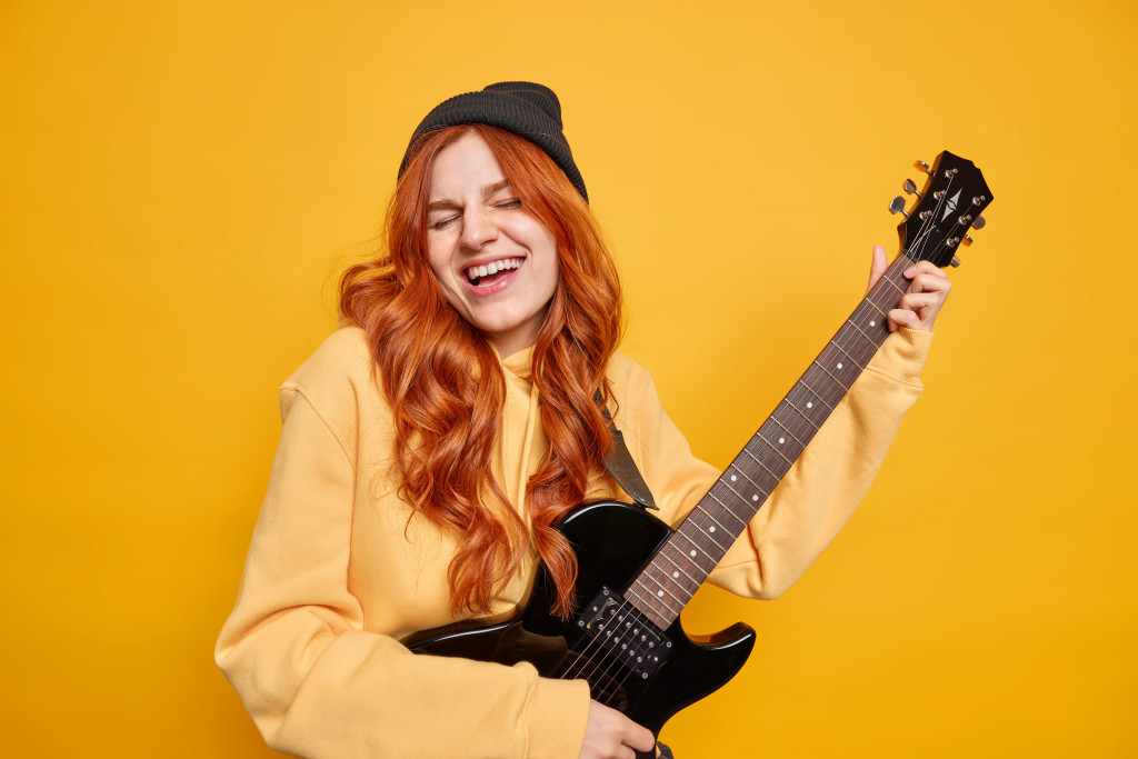 a happy redhead lady playing a guitar in front of a yellow backdrop