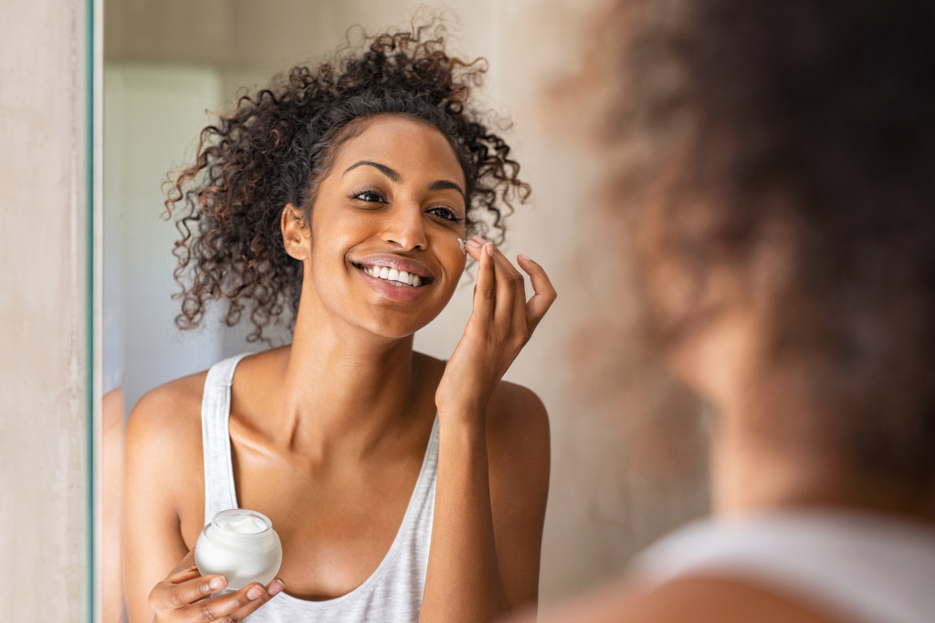 A beautiful woman applying cream on her face in front of a mirror