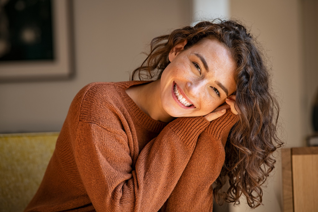 happy young woman sitting on sofa and looking at camera