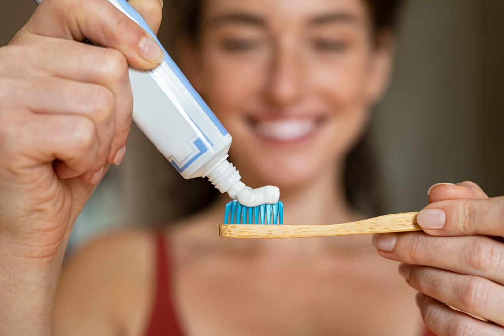 Young woman putting toothpaste on a wooden toothbrush.
