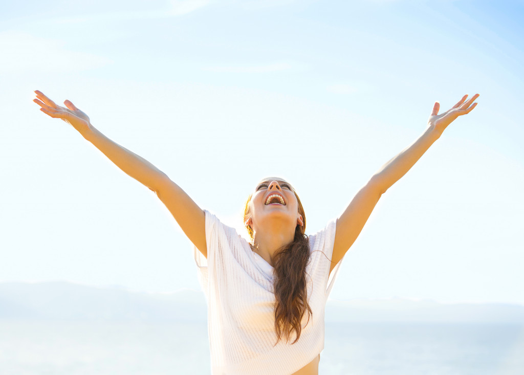 Woman smiling arms raised up to blue sky, celebrating freedom