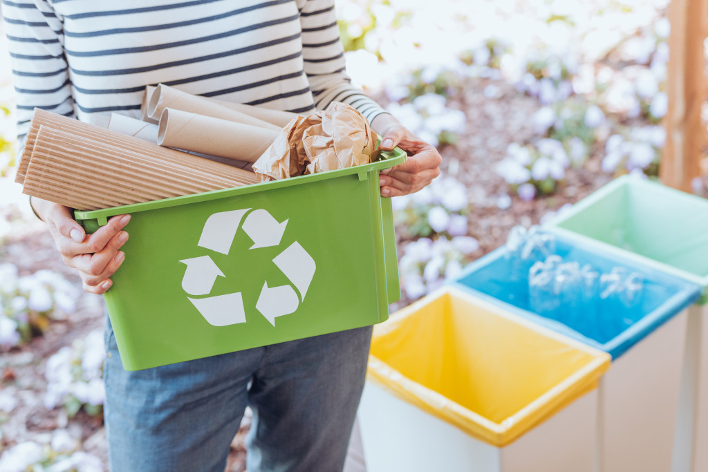 a woman holding a recycling bin beside separate trash bins