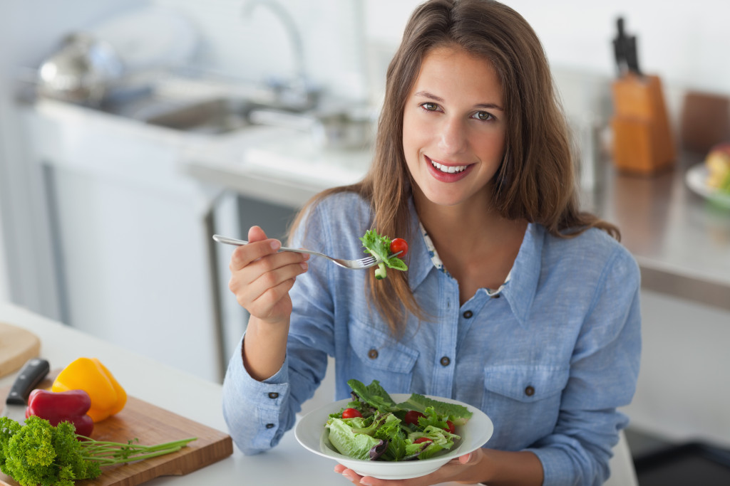 woman smiling while eating a leafy green salad in the kitchen