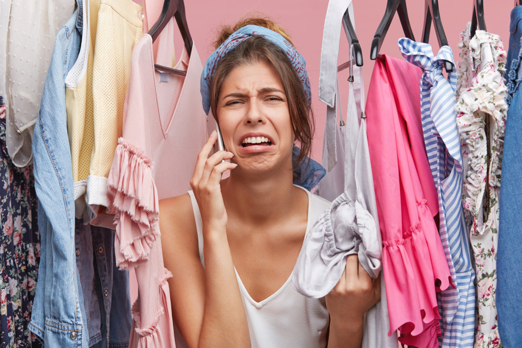 A woman making a call in the closet, in distress, not finding the perfect clothes to wear