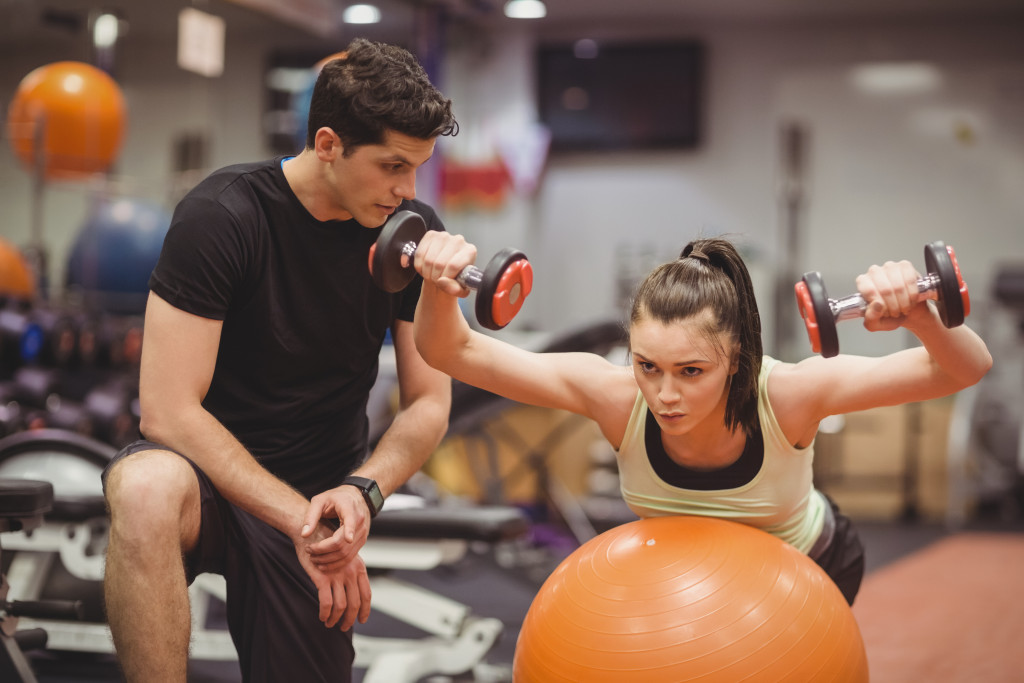 male personal trainer coaching a woman lifting in the gym