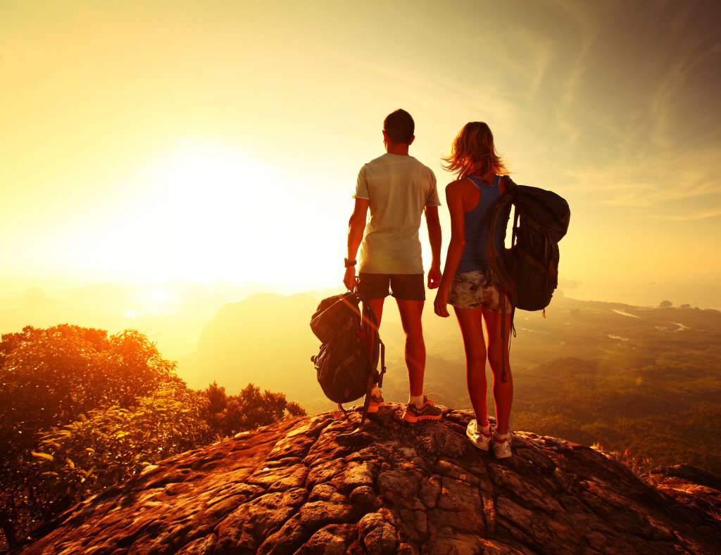 Young couple with backpacks enjoying the view from a mountain top during sunset.