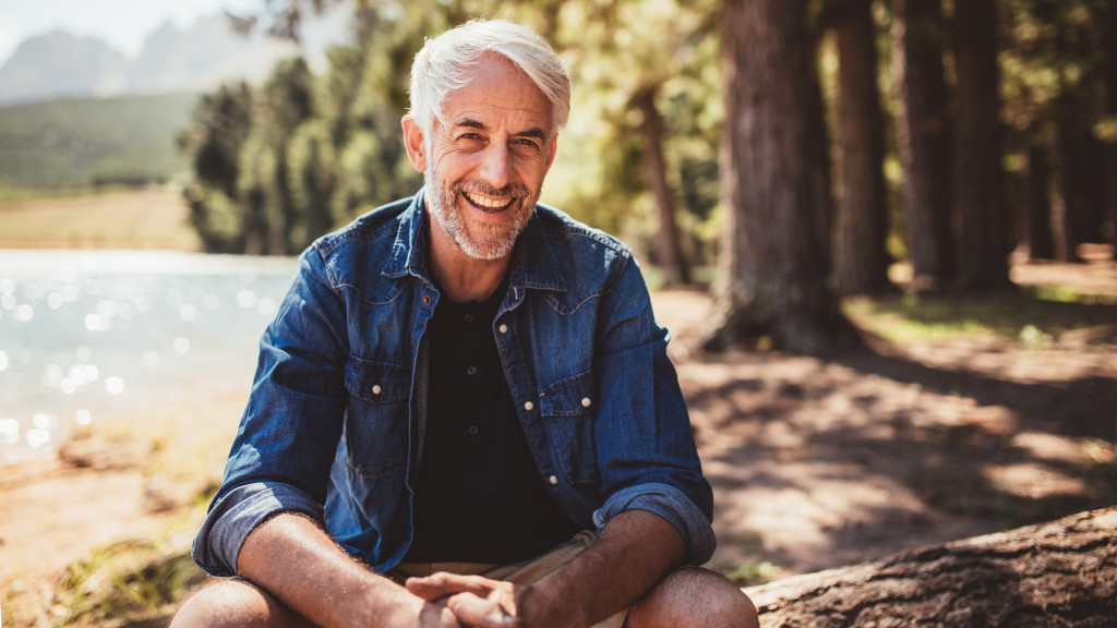 Mature man sitting on a log in the middle of a forest.