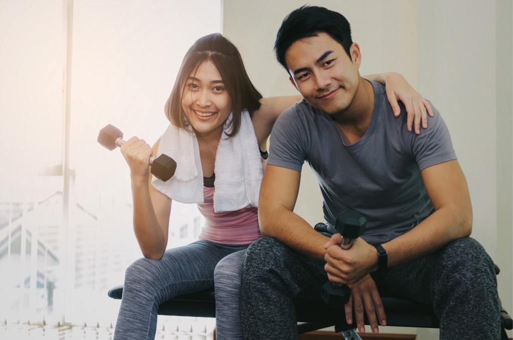 Young couple sitting on a bench with the woman exercising using a dumbbell.