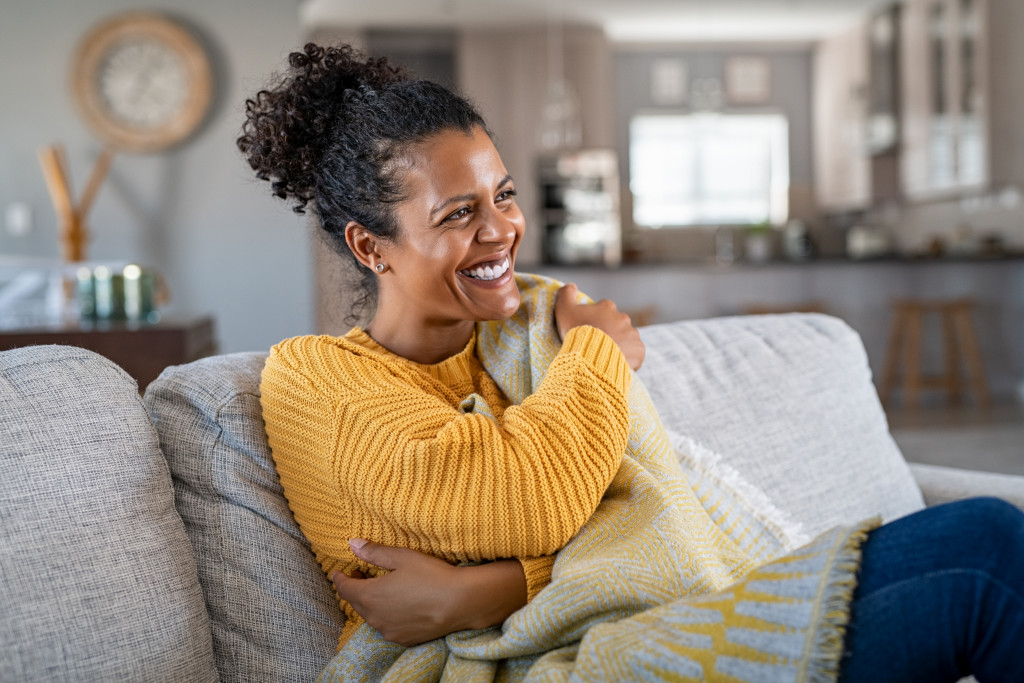 Young woman sitting on a couch while wrapping herself with a blanket.